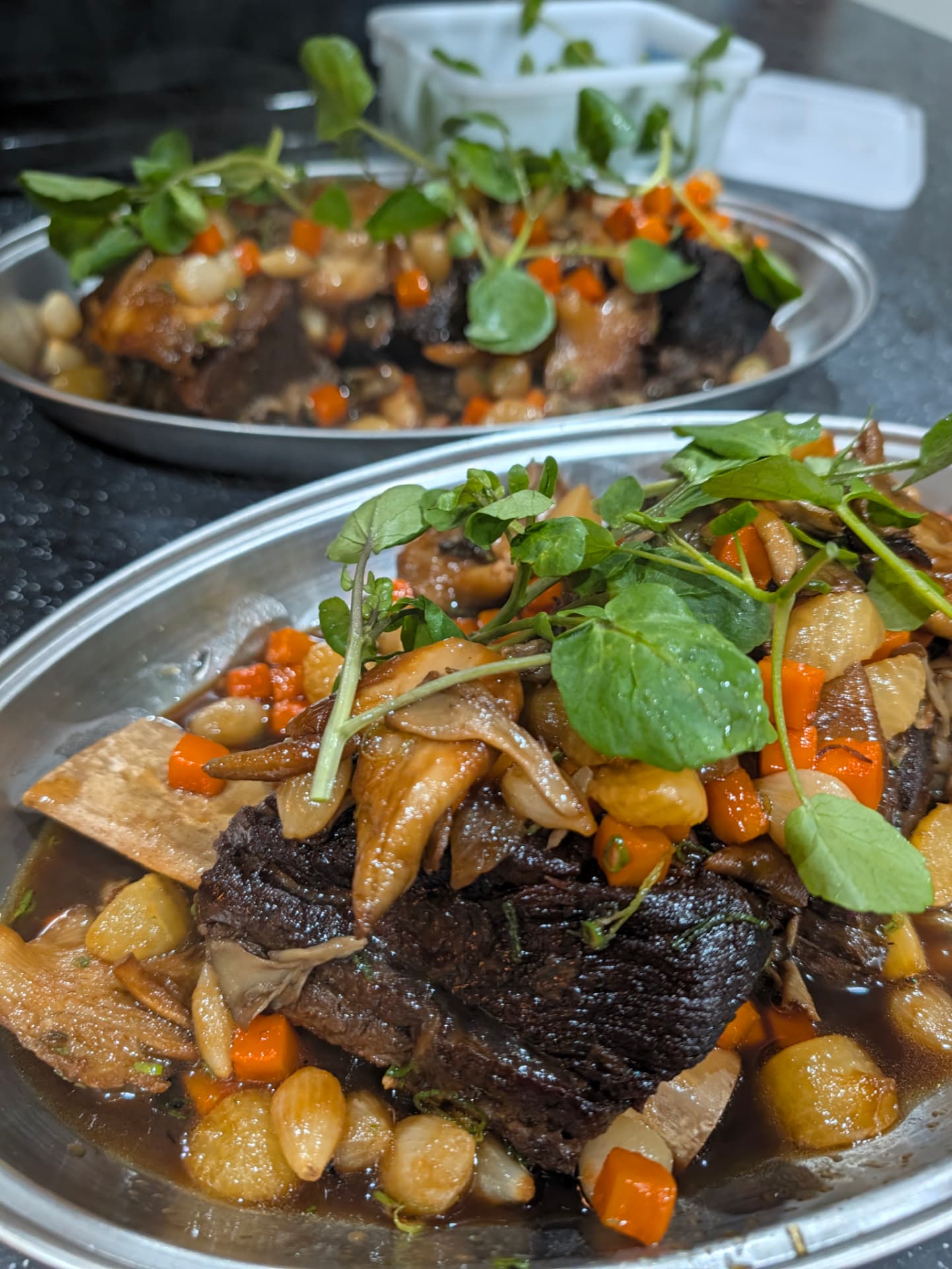 braised beef short ribs on serving platters with watercress, carrots and pearl onions