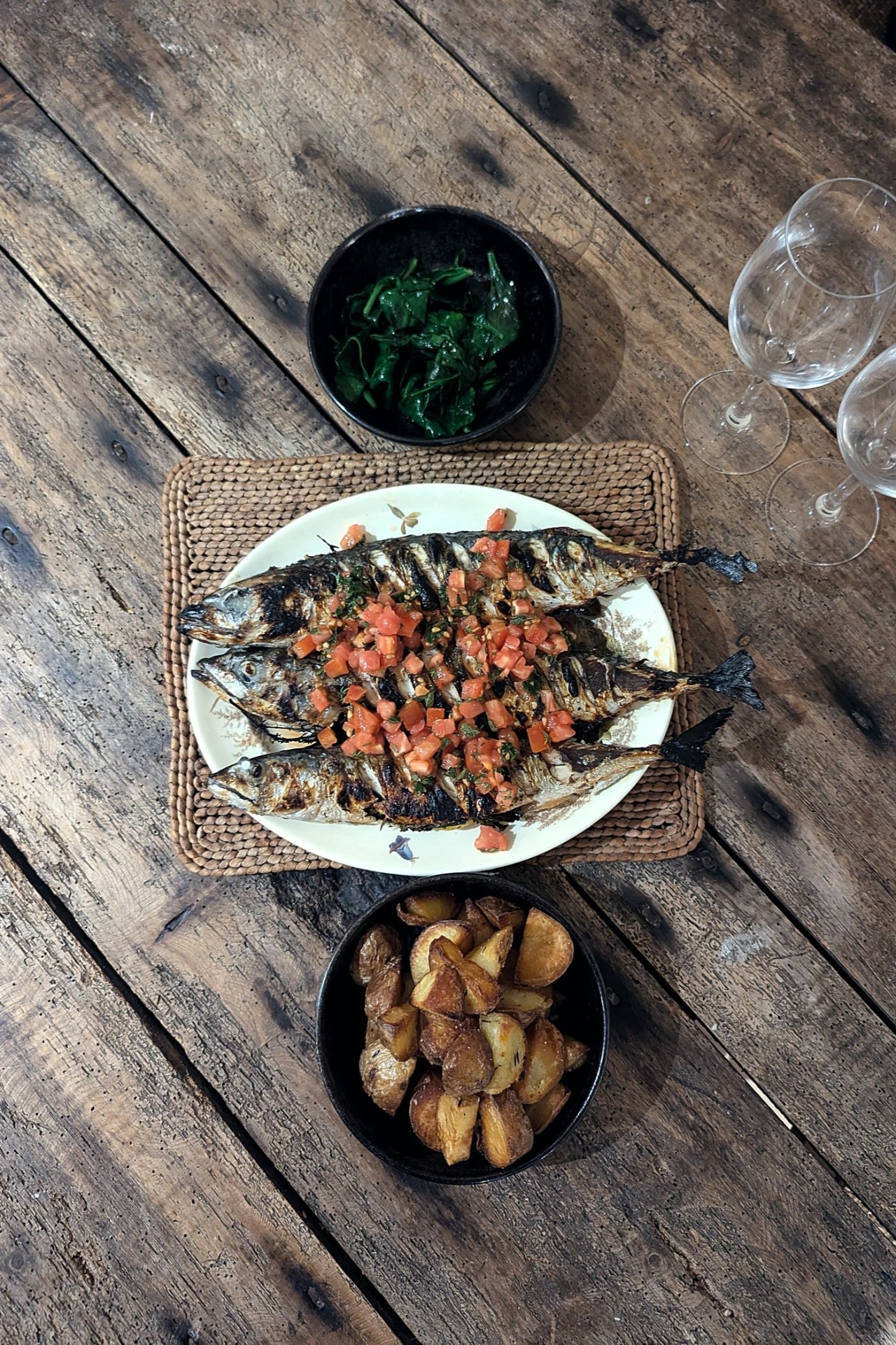 grilled mackerel with chopped tomato, wilted greens and roasted potatoes on a wooden table