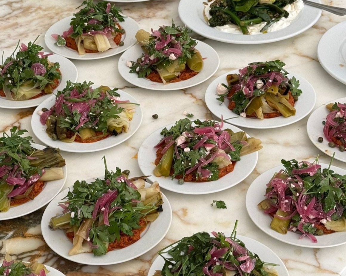 rows of plated starters with charred leeks, pink pickled onion, parsley and feta on a marble counter