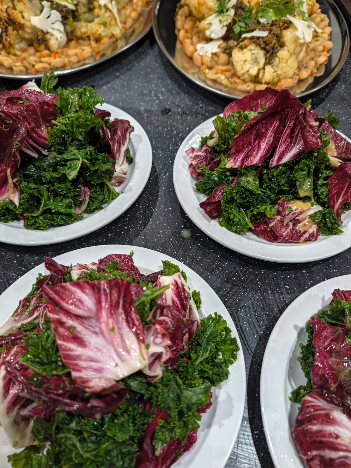 plates of kale and radicchio salad with platters of roasted cauliflower and white beans on a work surface